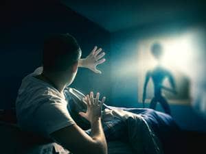 an alien in a room with a man on the bed scared