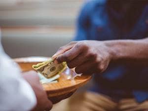 a person's hand putting money in a bowl paying tithing 