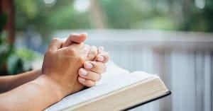 a woman has her hands clasped atop a Bible